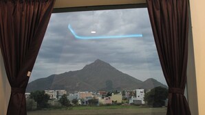 Vista a través de una ventana con cortinas, mostrando una montaña y edificios al fondo.