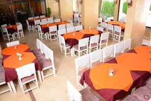 A banquet hall with multiple round tables covered with orange tablecloths and white chairs. - Shady hotel, Luxor downtown (Luxor Governorate)