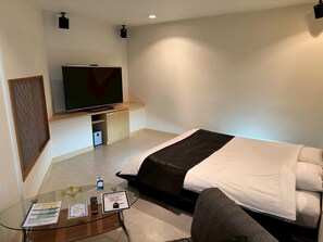 Habitación de hotel con cama, televisor, una mesita de vidrio y un televisor montado en la pared.