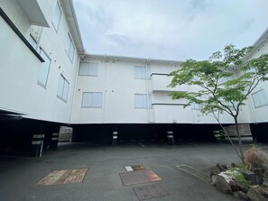 Un patio con un edificio, un árbol y una zona de estacionamiento.