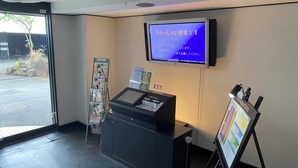 A reception area with a digital screen displaying text, a reception desk, a magazine rack, and an information stand.