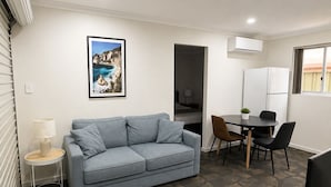 Un espace de vie compact comprenant un canapé, une table à manger avec des chaises, une petite table d’appoint, un téléviseur et un réfrigérateur.