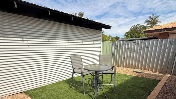 A patio with artificial grass, two metal chairs, and a table.