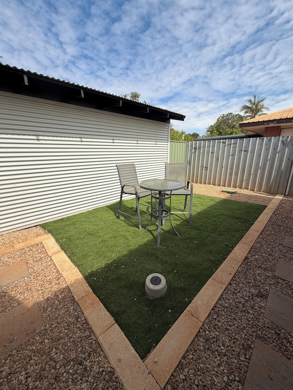 A patio with artificial grass, two metal chairs, and a table.