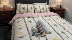 A neatly made bed with a floral pattern, two bedside lamps, a wall-mounted air conditioner, and a piece of wall art.