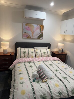 A neatly made bed with a floral pattern, two bedside lamps, a wall-mounted air conditioner, and a piece of wall art.