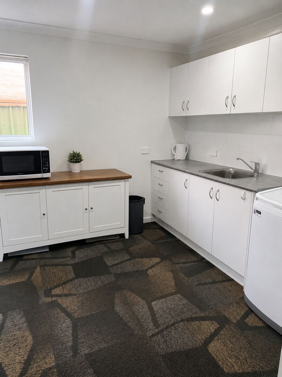 A modern kitchen with white cabinets, a microwave, a sink, and a small potted plant.