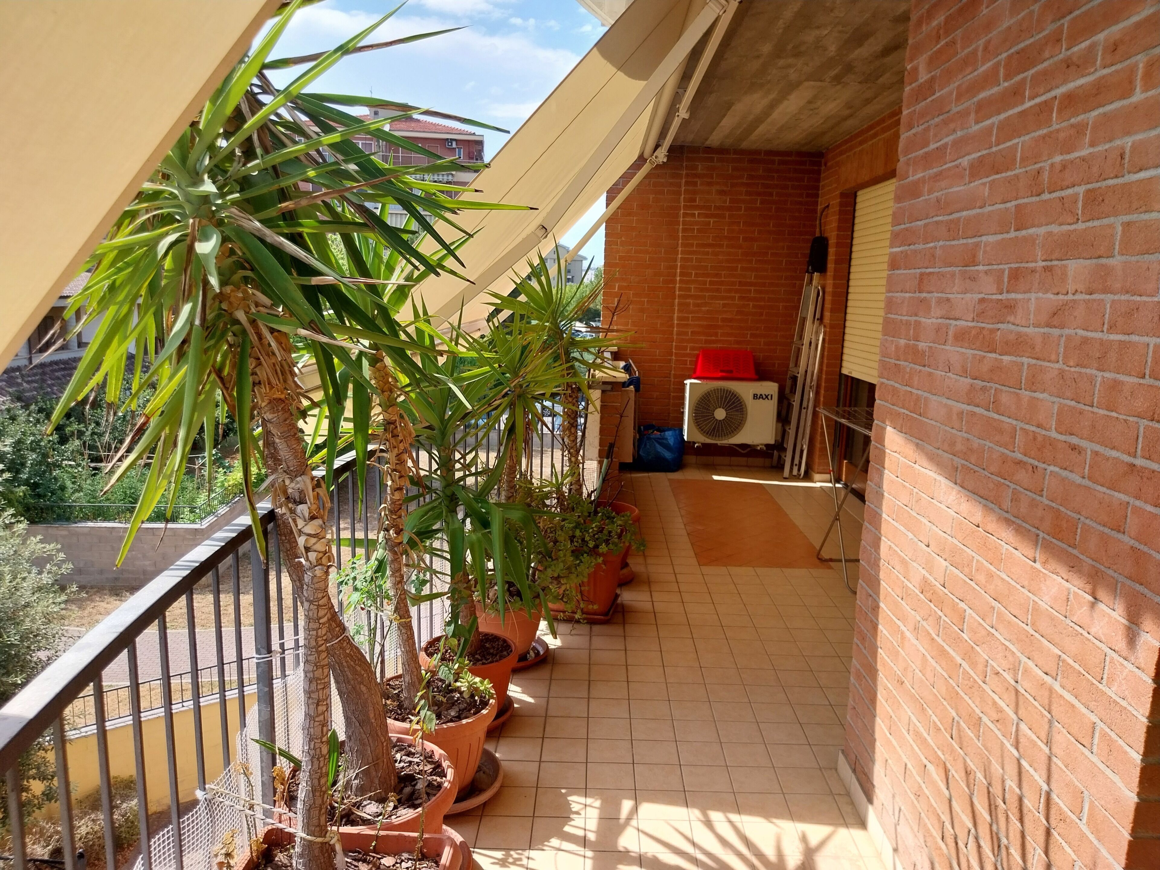 A balcony with potted plants, a red air conditioning unit, and a brick wall.