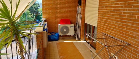 A balcony with a potted plant, a fan, and a drying rack.