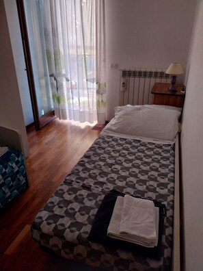 A bedroom with a bed, a nightstand with a lamp, a radiator, and a window with sheer curtains. - 
Feel right at home and relax just steps from the sea. (Pescara)