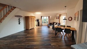 Een ruime woonkamer met houten vloer, een eettafel met stoelen, een bank en een trap.