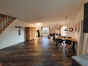 A spacious living area with a wooden floor, a dining table with chairs, a sofa, and a staircase. - Op'n Rugenbarg Vacation Rental Ebbe H60 (Cuxhaven)