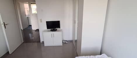 Habitación de hotel con dos camas, televisión, armario y baño visible a través de una puerta abierta.