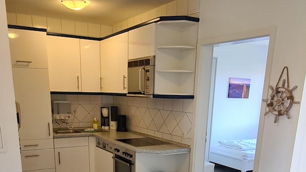 A compact kitchen with white cabinets, a built-in oven, and a microwave. - Op'n Rugenbarg Vacation Rental Elbe H64 (Cuxhaven)
