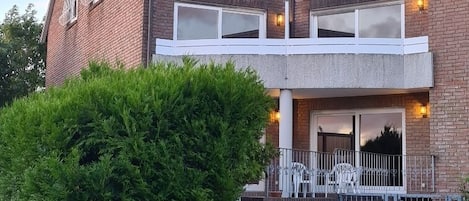 Un immeuble résidentiel de deux étages avec une façade en briques, un balcon à l’étage supérieur et une pelouse bien entretenue.