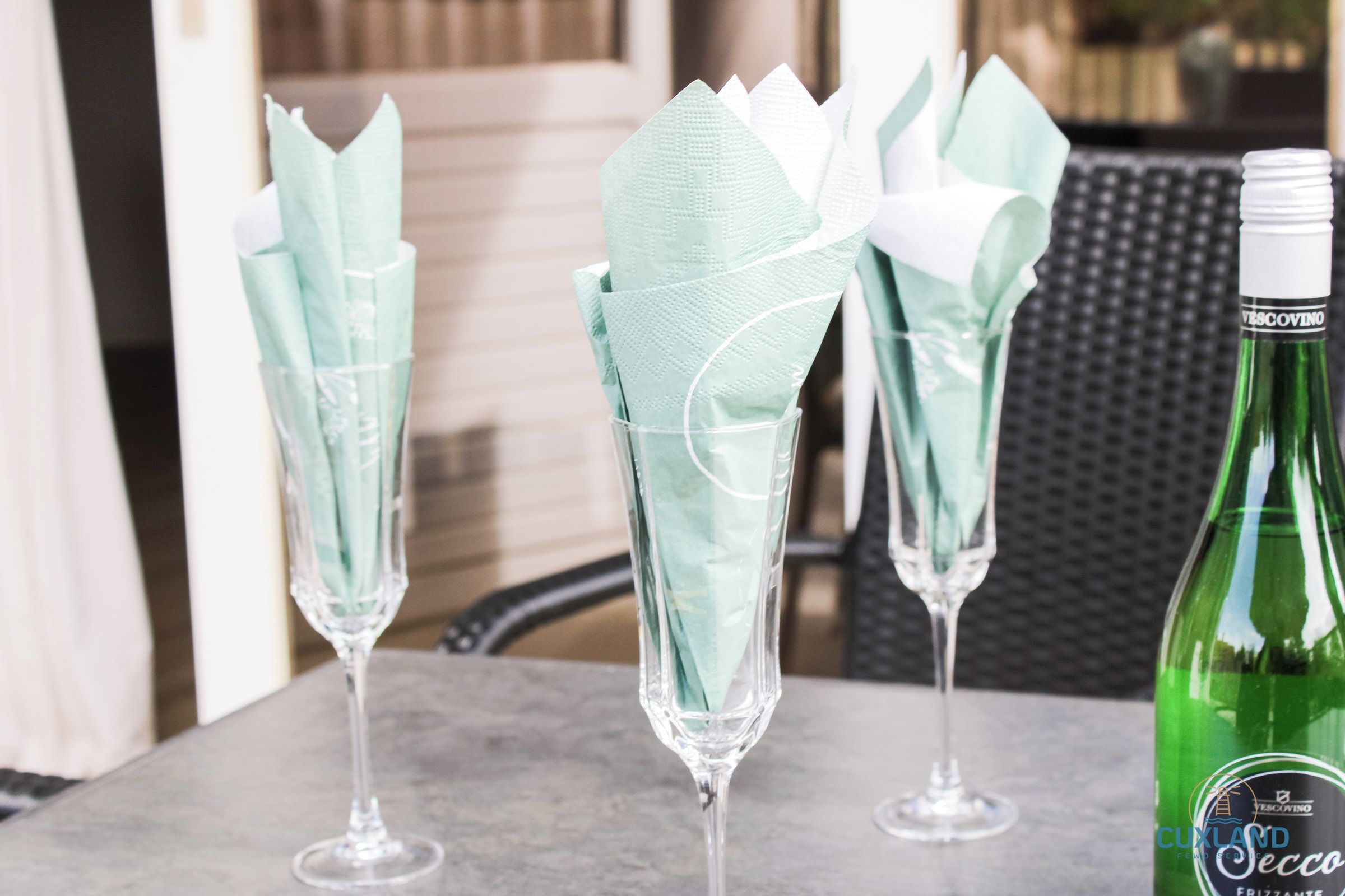 Tre champagneglas med servietter, en flaske Secco og en sort stol.