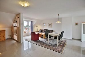 A spacious living area with a dining table, chairs, and a red ottoman. - "Sturmflut" Vacation Rental on the Rugenbarg (Cuxhaven)