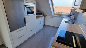 A compact kitchen with a built-in oven, microwave, and a window above the sink. - "Sturmflut" Vacation Rental on the Rugenbarg (Cuxhaven)