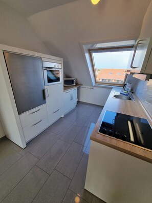 A compact kitchen with a built-in oven, microwave, and a window above the sink. - "Sturmflut" Vacation Rental on the Rugenbarg (Cuxhaven)