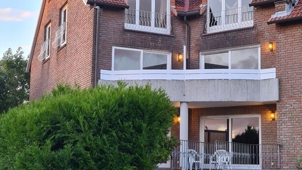 A two-story brick house with a balcony, a small garden, and a visible door. - "Sturmflut" Vacation Rental on the Rugenbarg (Cuxhaven)
