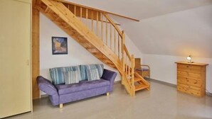 A room with a wooden staircase, a purple sofa, and a wooden cabinet. - "Sturmflut" Vacation Rental on the Rugenbarg (Cuxhaven)