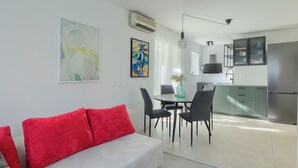 A modern living room with a sofa, a dining table with chairs, and a kitchen area with cabinets and a refrigerator. - Fortica Garden Apartment – Pula Arena, Free Parking (Pula)