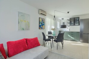 A modern living room with a sofa, a dining table with chairs, and a kitchen area with cabinets and a refrigerator. - Fortica Garden Apartment – Pula Arena, Free Parking (Pula)