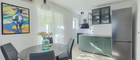 A modern kitchen with a stainless steel refrigerator, a dining area with a round table and chairs, and a colorful abstract painting on the wall.