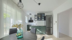 A modern kitchen with a built-in oven, a stainless steel refrigerator, and a dining area with a round table and chairs. - Fortica Garden Apartment – Pula Arena, Free Parking (Pula)