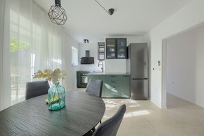 A modern kitchen with a built-in oven, a stainless steel refrigerator, and a dining area with a round table and chairs. - Fortica Garden Apartment – Pula Arena, Free Parking (Pula)