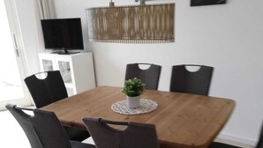 A dining area with a wooden table, six chairs, a small potted plant, and artwork on the wall. - Op'n Rugenbarg Vacation Rental, Wadden Sea, H62 (Cuxhaven)