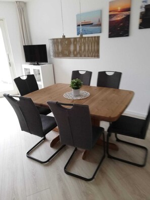 Ein Essbereich mit einem Holztisch, sechs Stühlen, einem kleinen Topfpflanzen und Kunstwerken an der Wand.