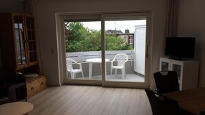 A room with a sliding glass door leading to an outdoor balcony, a television on a cabinet, and a dining table with chairs. - Op'n Rugenbarg Vacation Rental, Wadden Sea, H62 (Cuxhaven)
