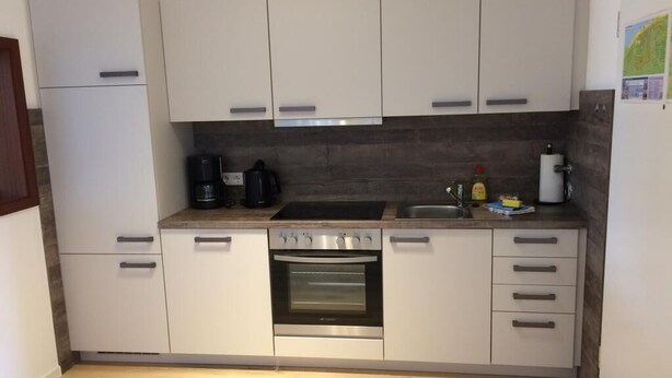 A compact kitchen with white cabinets, a built-in oven, a coffee maker, and a sink. - Op'n Rugenbarg Vacation Rental, Wadden Sea, H62 (Cuxhaven)