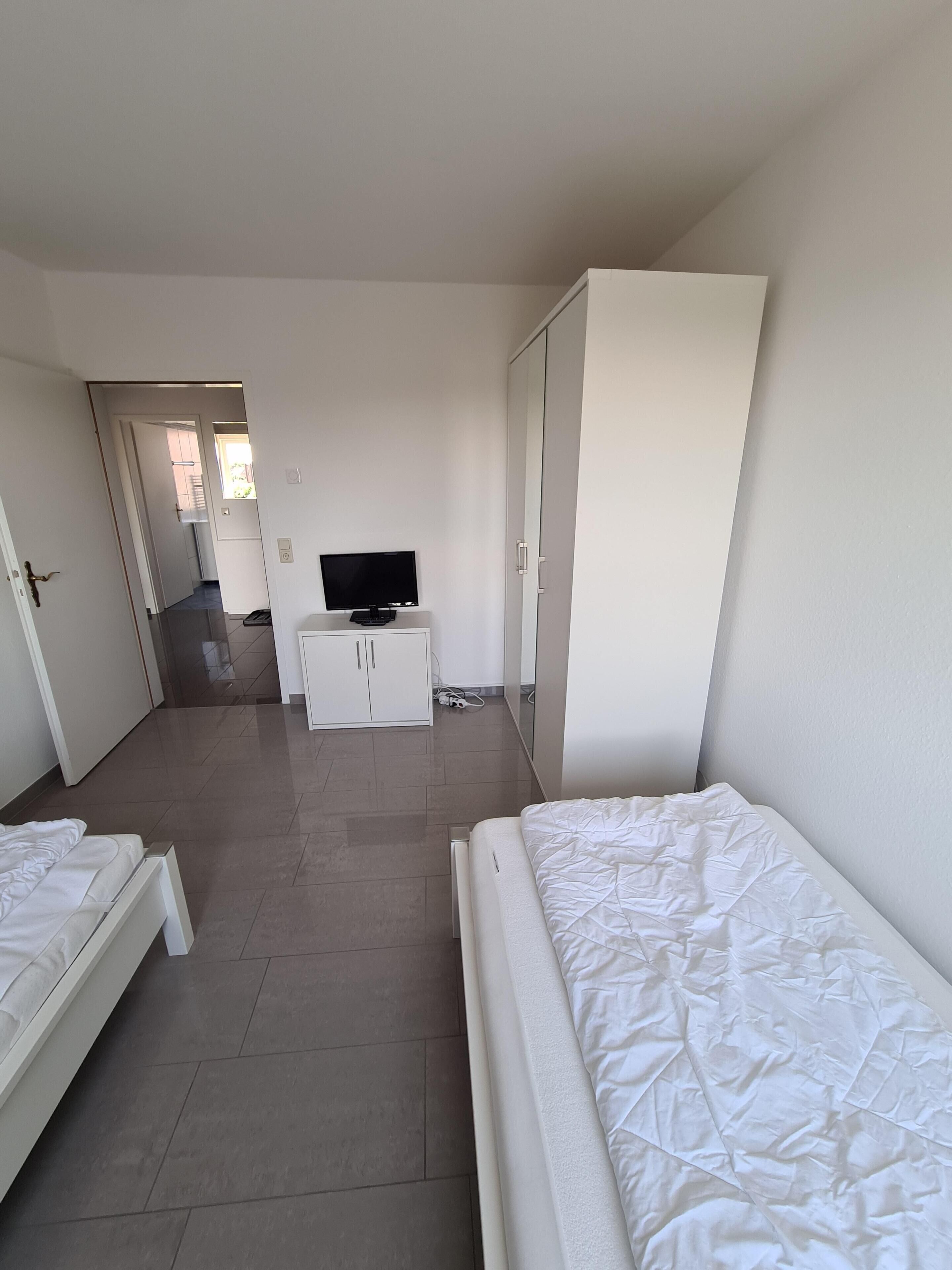 Ein Hotelzimmer mit zwei Betten, einem Fernseher, einem Kleiderschrank und einem durch eine offene Tür einsehbaren Badezimmer.
