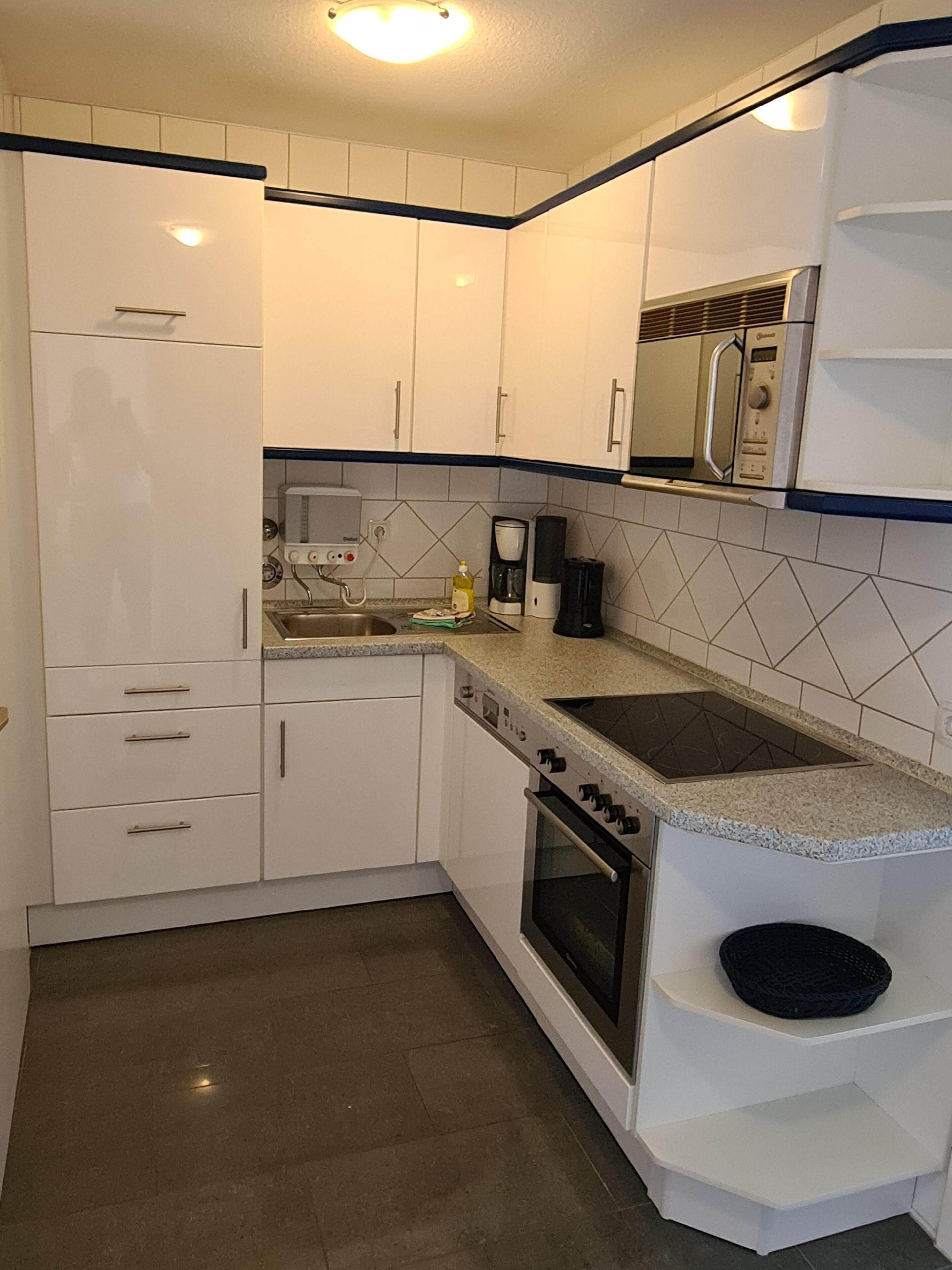 A kitchen with white cabinets, a built-in oven, a microwave, and a coffee maker.