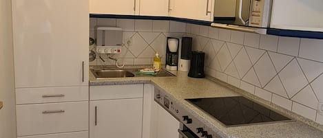 Una cocina con gabinetes blancos, horno empotrado, microondas y cafetera.