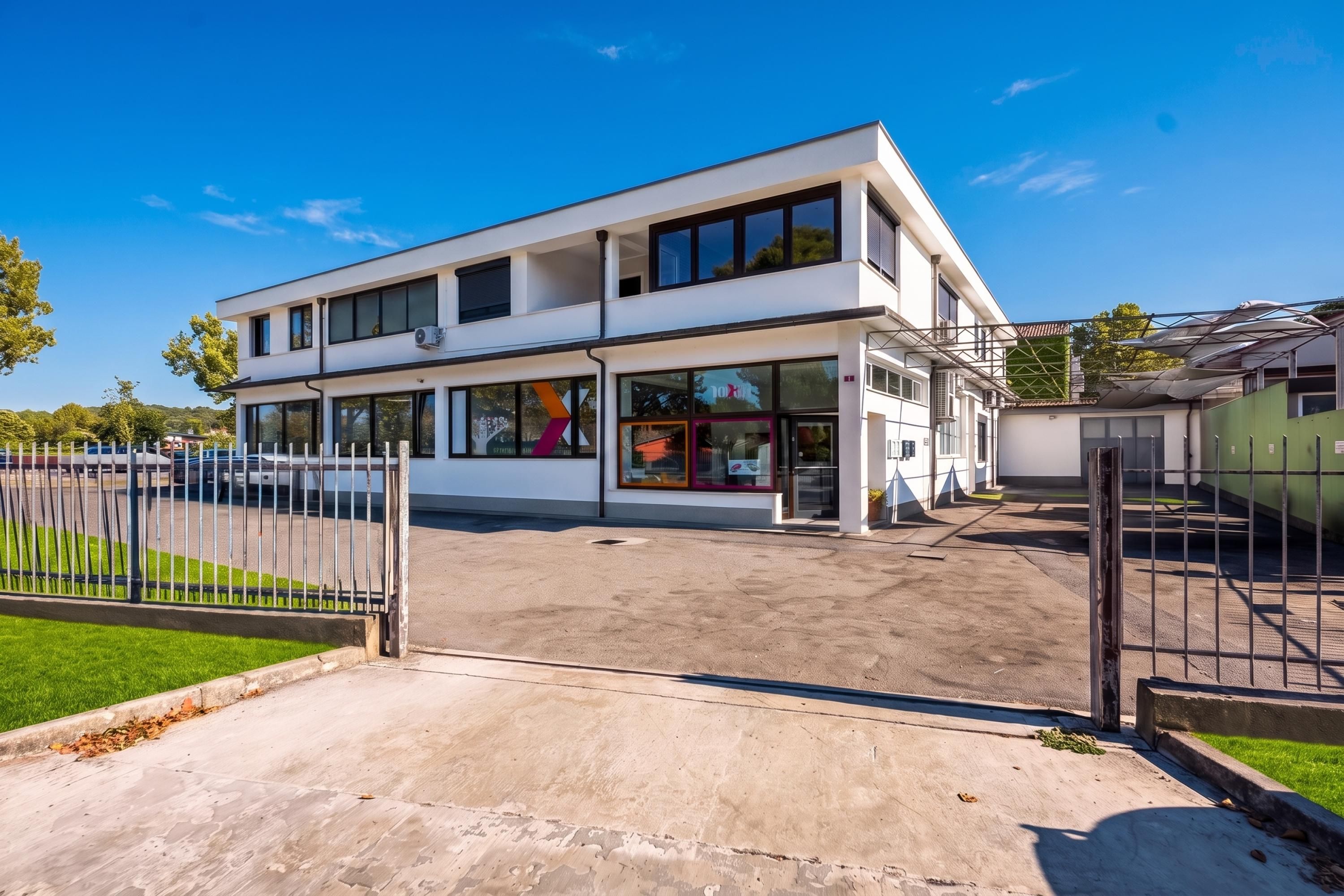A modern two-story building with a flat roof, large windows, and a gated entrance.