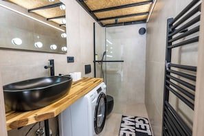 A compact bathroom with a wooden vanity, a black sink, a washing machine, and a glass shower enclosure. - Alter 26 Urban Apartment With Free Parking (Koper)