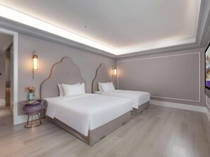 Una habitación de hotel moderna con dos camas, una mesita redonda con un florero y un televisor en la pared.