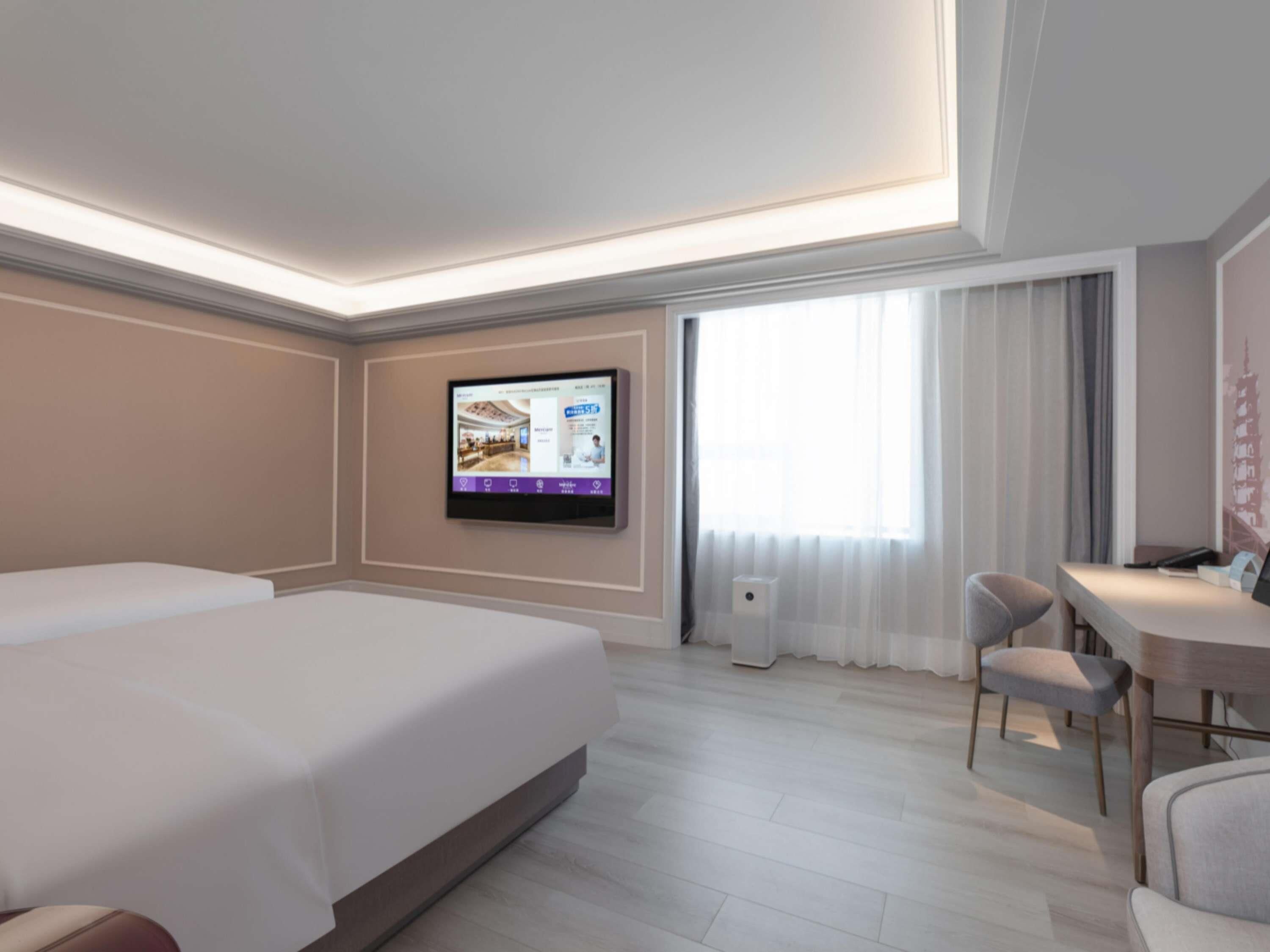 Habitación de hotel con cama, escritorio, silla, televisor montado en la pared y ventana con cortinas.