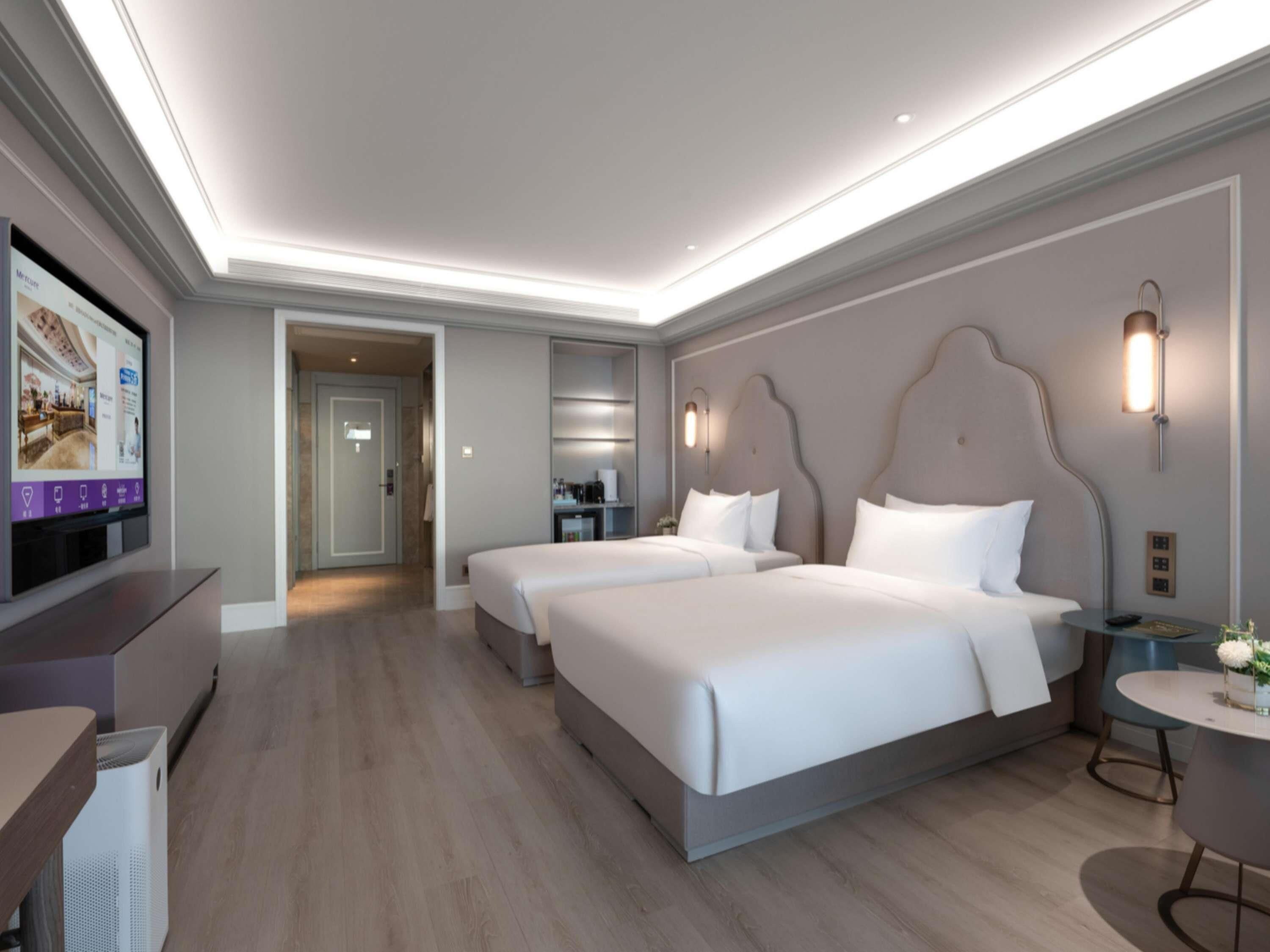 A hotel room with two beds, a TV, a desk, and a small round table.
