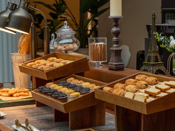 A buffet table with various pastries and desserts, a candle, and a decorative Eiffel Tower model.
