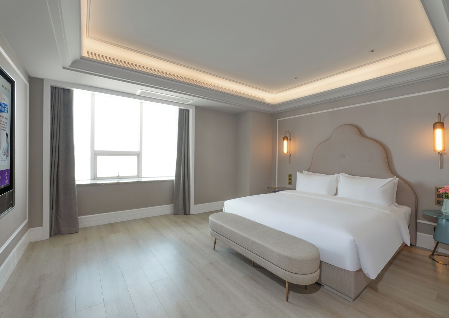 A hotel room with a large bed, a bench, a TV, and a window with curtains.