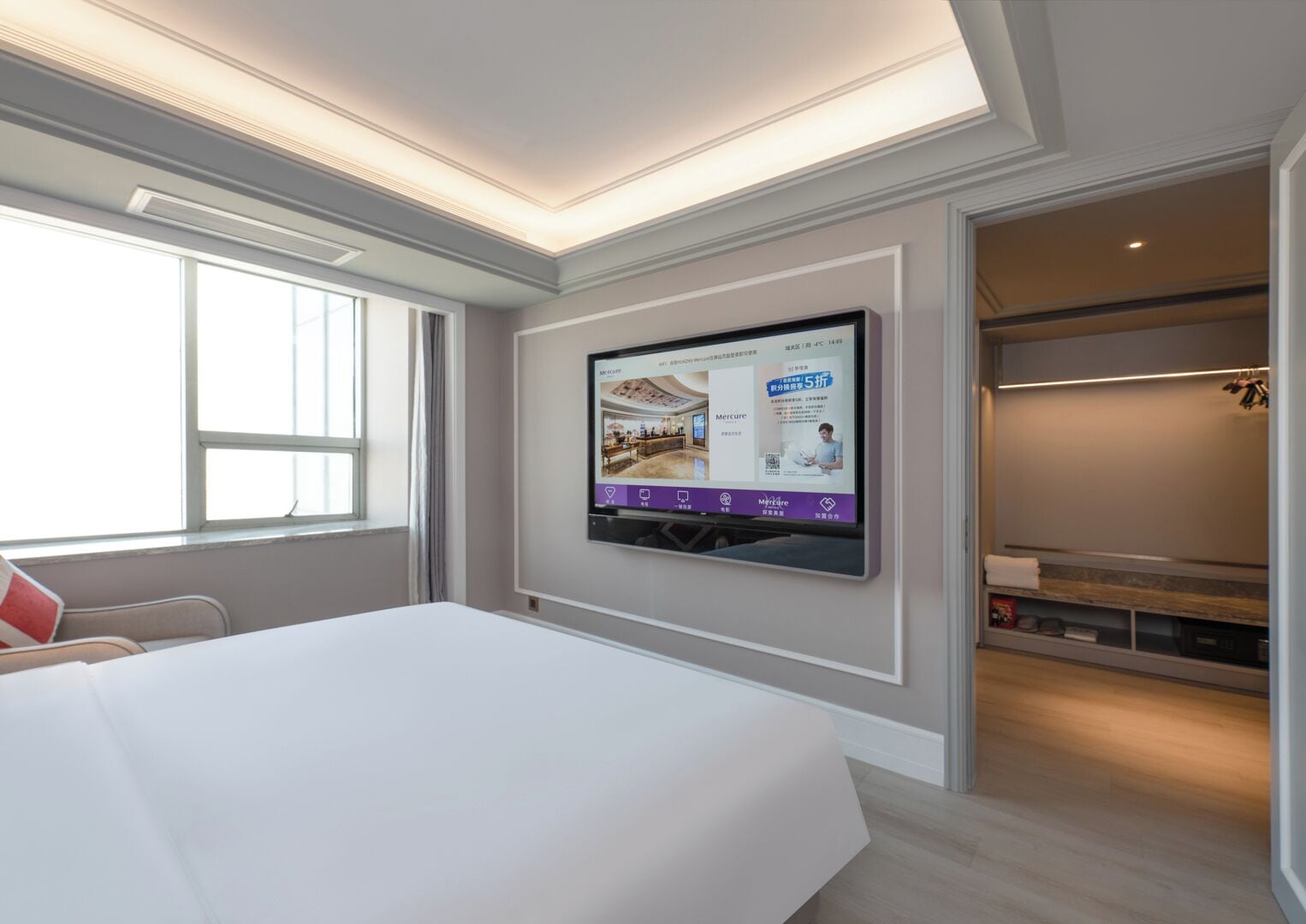 Ein Hotelzimmer mit einem großen Bett, einem an der Wand montierten Fernseher und einem Fenster, das natürliches Licht hereinlässt.