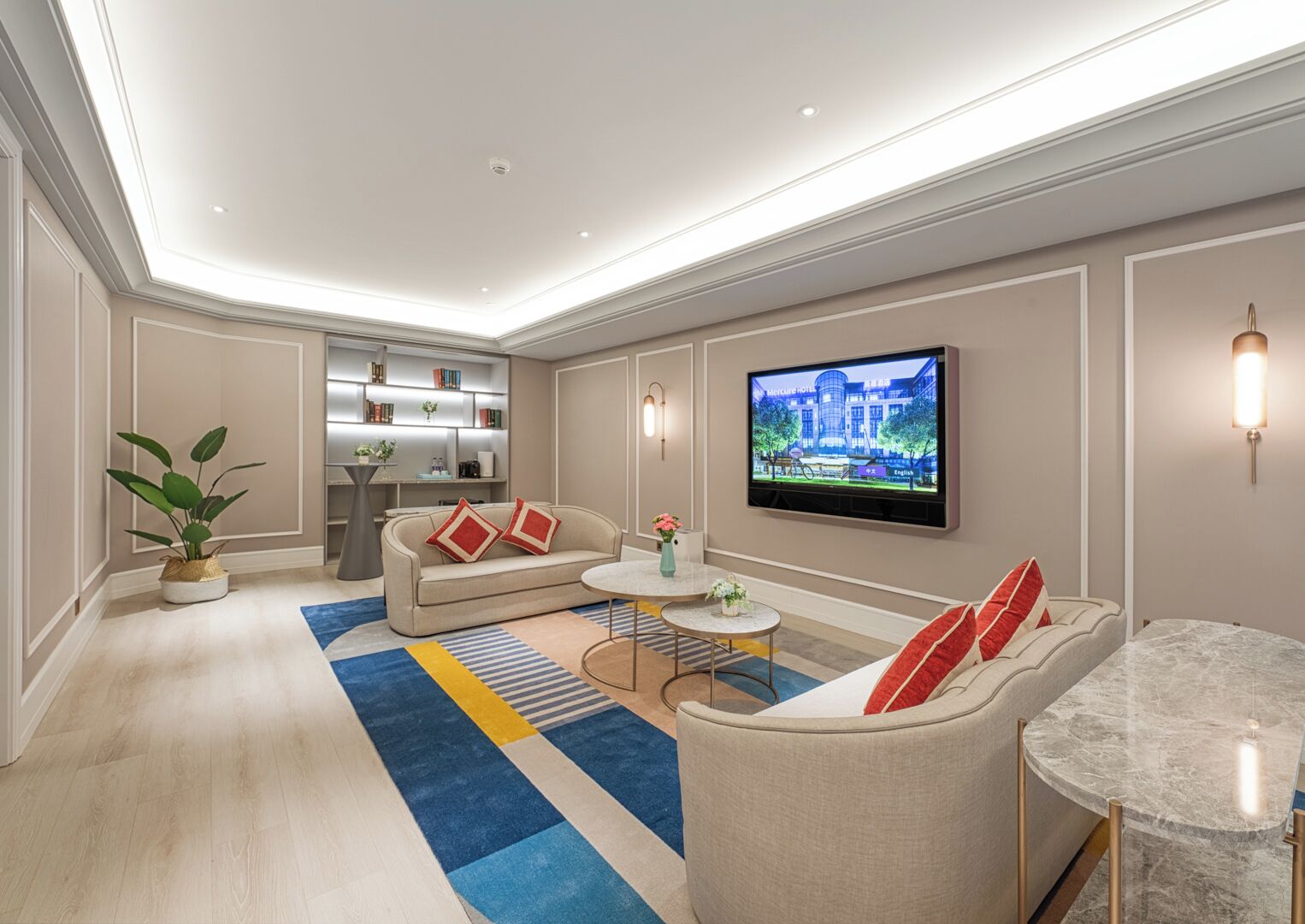 A modern hotel room with a flat-screen TV, a sofa, a coffee table, and a small dining table.