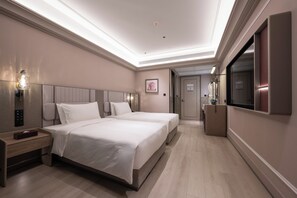 Habitación de hotel con dos camas, una mesita de noche, televisión y puerta de baño.
