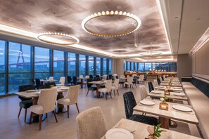 A spacious dining area with high ceilings, large windows, and modern lighting fixtures. - Mercure Shanghai Lujiazui Binjiang Center (Shanghai)