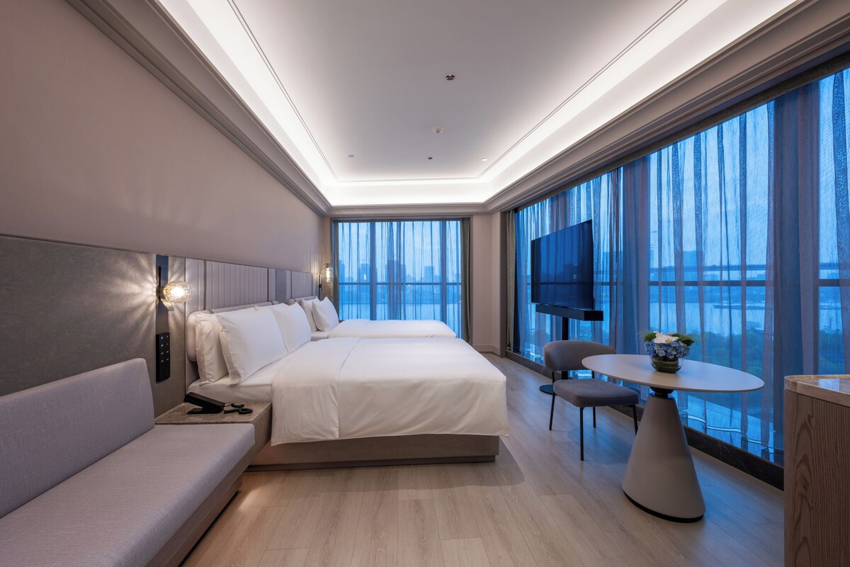 A modern hotel room with a large bed, a sofa, a dining table, and a TV.