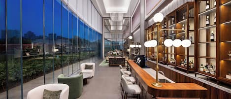 A modern bar area with a high ceiling, large windows, and a wine display.